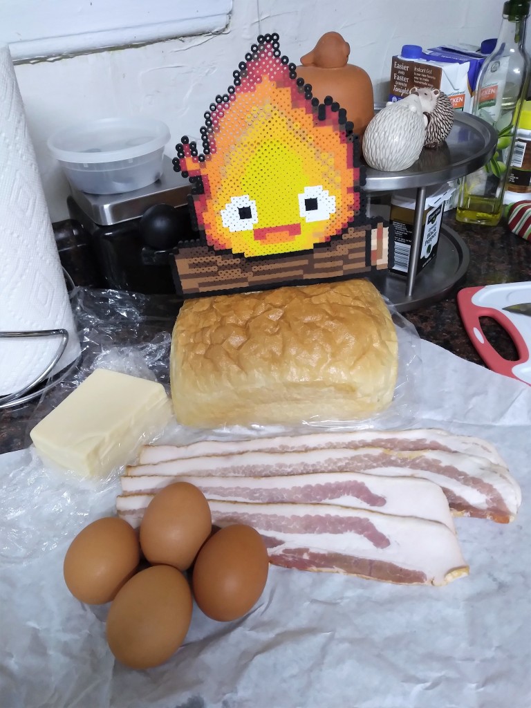 Eggs, bacon, bread, and butter displayed in the foreground with a perler bead Calcifer in the background