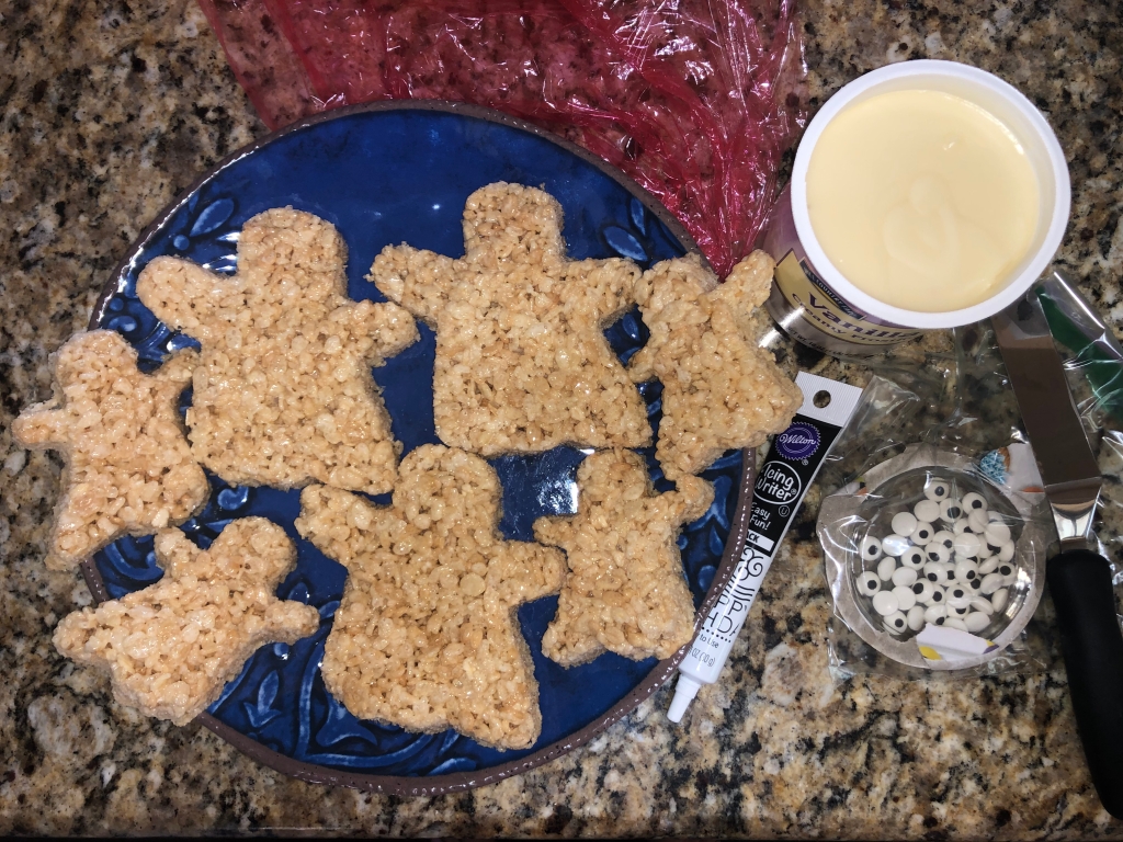 Ghost-shaped Rice Krispies treats on a plate with vanilla icing, white icing writer, and edible eyeballs 