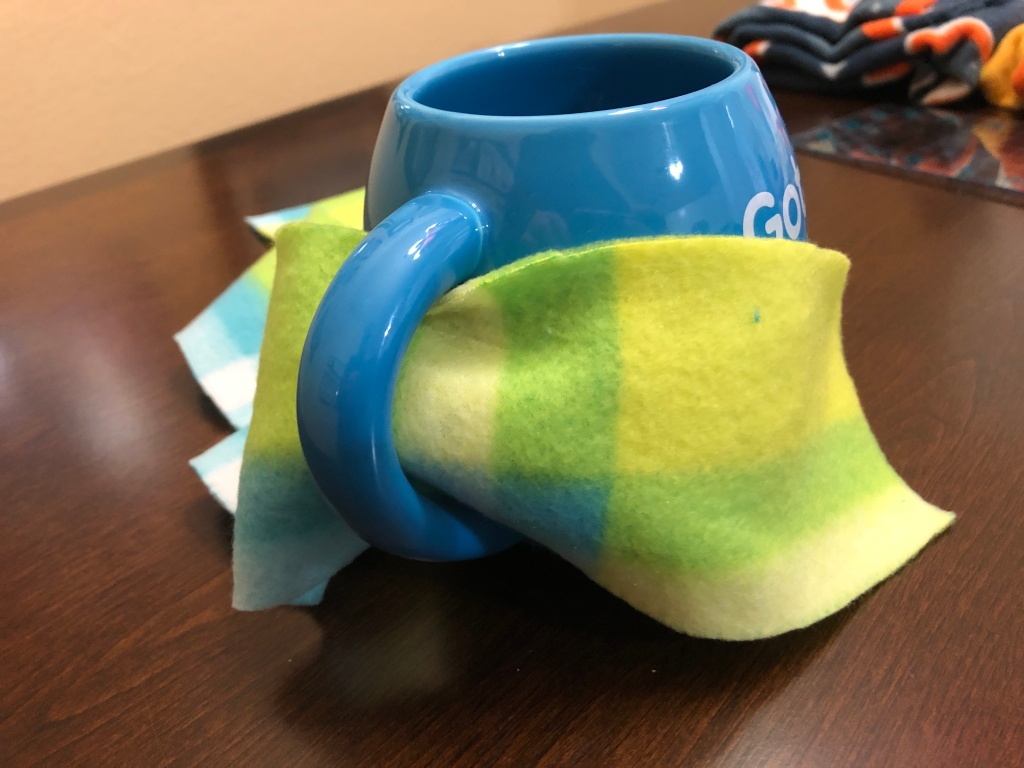 Close-up of the blue mug with DIY fleece koozie wrapped around it and under the mug handle.